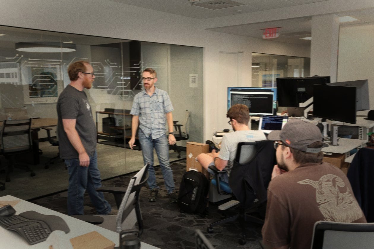 Two engineers talking beside a desk in the Code Metal office